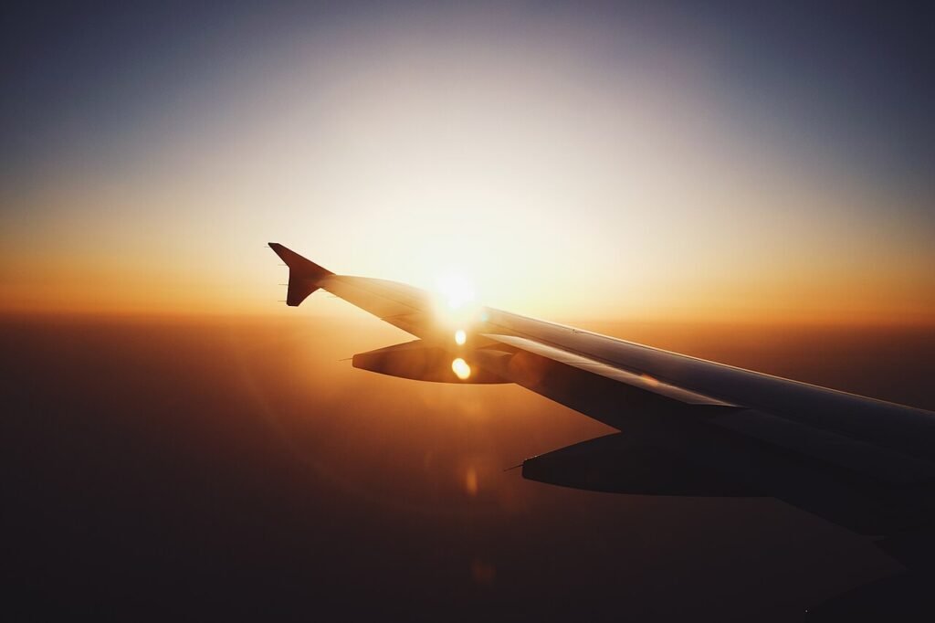 View of an airplane wing over clouds at sunset, worldwide flights