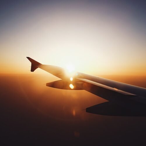 View of an airplane wing over clouds at sunset, worldwide flights