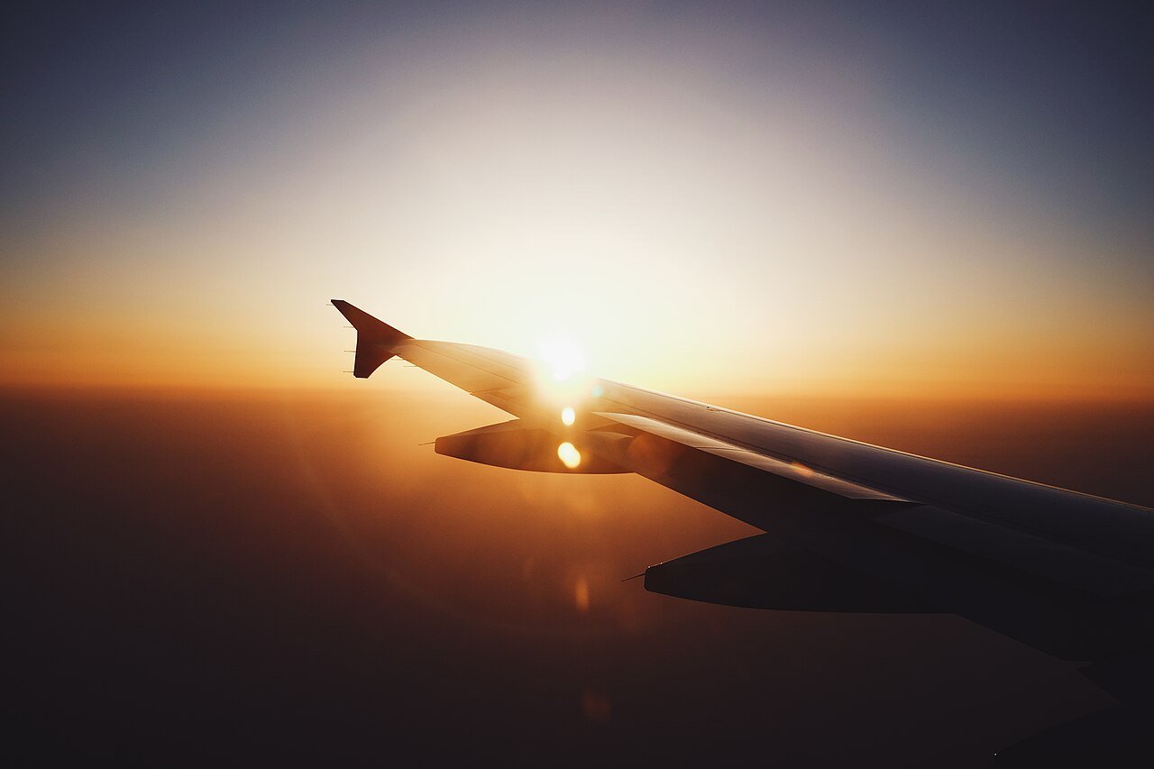 View of an airplane wing over clouds at sunset, worldwide flights